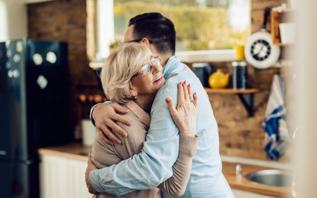 Happy senior woman embracing her adult son in the kitchen.